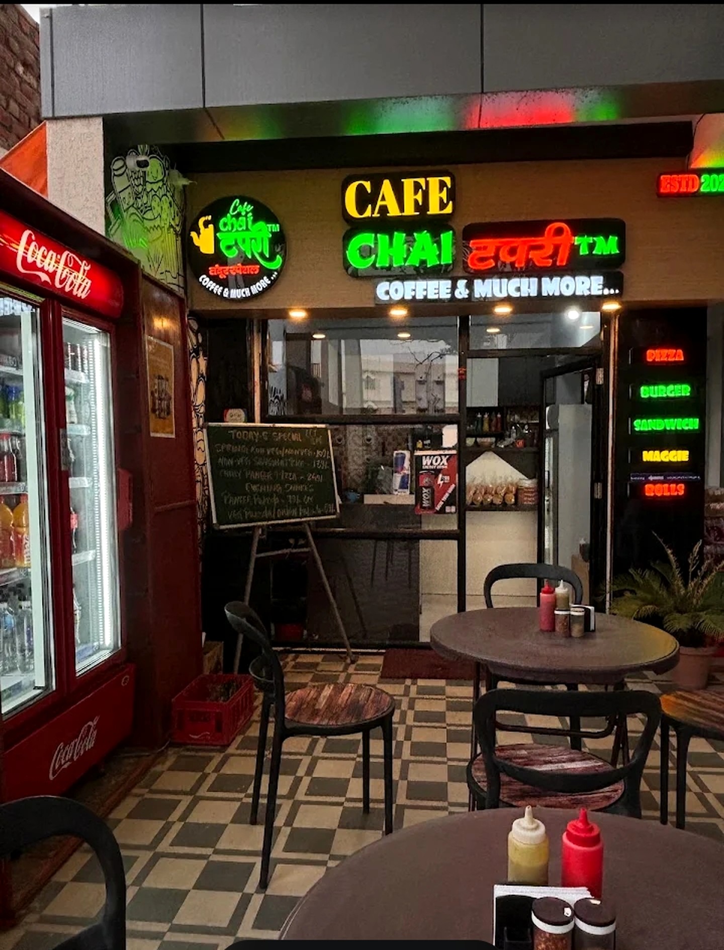 Seating area inside Cafe Chai Tapri with checkered floor, round tables and the restaurant's glowing signboard